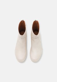 Botines de cuero blanco con una textura suave, punta redondeada y un interior marrón en contraste. Presentan un cierre de cremallera lateral.