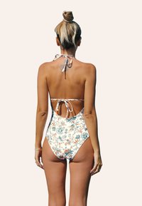 Costume da bagno intero color crema con motivi floreali in arancione e teal, dotato di una scollatura all'americana con nodo, schiena scoperta e bretelle regolabili.
