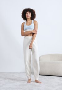 Sujetador deportivo ligero con rayas en azul y blanco, combinado con pantalones de chándal suaves en color crema que cuentan con una cinturilla elástica y piernas ajustadas.