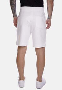 Shorts bianchi in cotone con vita elasticizzata, dotati di una tasca posteriore singola e di un orlo rifinito. Indossati con scarpe da ginnastica bianche.
