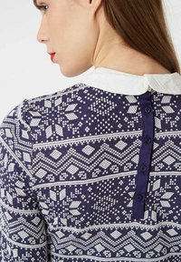 Mujer que lleva un suéter patrón en azul marino y blanco con un cuello Peter Pan blanco y cierre de botón en la parte de atrás.