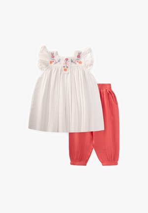 White cotton top with floral embroidery and ruffled sleeves paired with coral-colored, elastic-waist, tapered pants. Textured fabric.