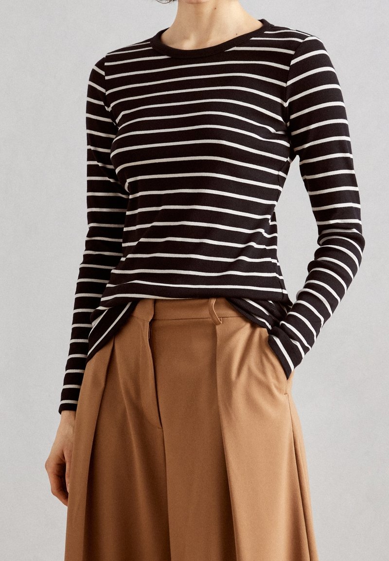 Camicia a maniche lunghe a righe bianche e nere con scollatura a girocollo, realizzata in tessuto morbido e testurizzato, abbinata a pantaloni beige a vita alta.