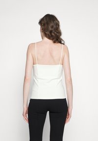 Débardeur ajusté blanc à fines bretelles, avec un dos carré et une texture lisse. Associé à un pantalon noir ajusté.