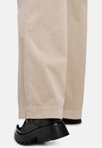 Beige corduroy trousers with wide legs, featuring a ribbed texture and a straight hem, paired with shiny black platform shoes.