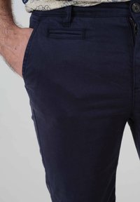 Pantalons bleu marine en coton, présentant une texture lisse, des poches latérales, une fermeture à bouton et une poche arrière discrète.