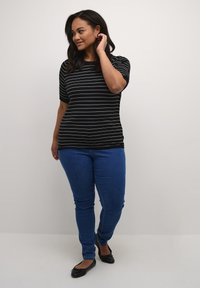 Top a righe bianche e nere con maniche corte, abbinato a jeans skinny blu e ballerine nere. Design semplice e aderente.