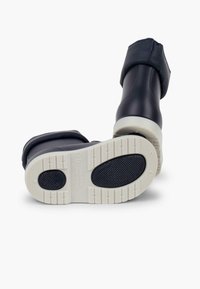 Botas de goma negras con suelas blancas. El diseño presenta una punta redondeada, una superficie texturizada y un puño para mayor cobertura.