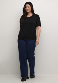Top negro de manga corta con escote redondo, combinado con vaqueros rectos de color azul oscuro. La modelo lleva zapatos de plataforma negros. Texturas simples y suaves.