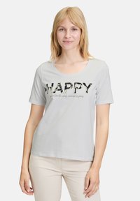 Grijze t-shirt met korte mouwen en een ronde halslijn. Kenmerkt zich door het woord "HAPPY" in een patroonprint, vergezeld van een kleinere tekst eronder.