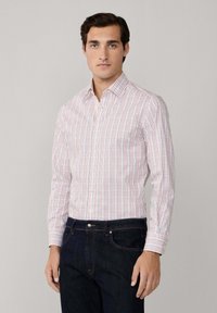 Chemise blanche à motif à carreaux rouges et bleus, col boutonné, manches longues, design ajusté. Associée à un jean en denim foncé.