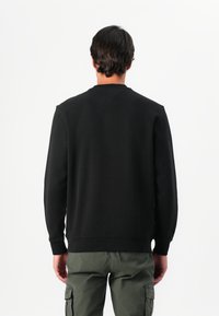 Zwart sweatshirt met een ronde hals, lange mouwen en geribbelde manchetten. Materiaal lijkt zacht en textuur te hebben. Draagt bij olijfgroen cargobroek.