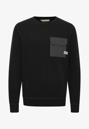 Melna sporta krekla, kas izgatavots no teksturēta auduma, ar pelēku kabatu kreisajā krūtī, apaļu kakla izgriezumu, kā arī ribota rezerves un apakšmalu.