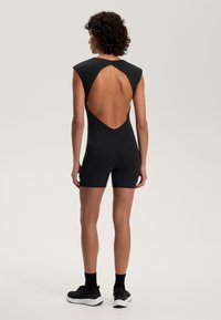 Zwart bodysuit met korte mouwen en een diepe uitsnijding op de rug, met een aansluitend ontwerp en een gladde textuur, gecombineerd met zwarte sportschoenen.