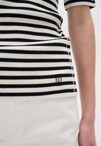 Nahaufnahme einer Person, die ein schwarz-weiß gestreiftes Ripptop und weiße Hose trägt, wobei ein Teil des Arms und des Oberkörpers zu sehen ist.