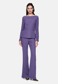 Purple two-piece suit featuring a structured top with a diagonal seam and flared pants. The fabric has a subtle shimmer.