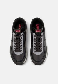 Black and gray sneakers with a textured finish, featuring round laces, a cushioned tongue, and a white rubber sole. Red Camper logo on the tongue.