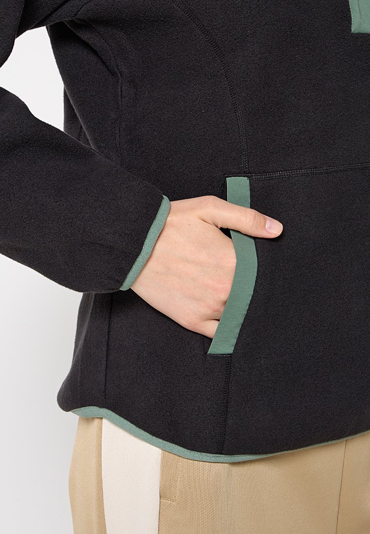Zwarte fleecejack met groene accenten; beschikt over een zijzak en contrasterende manchetten. Zachte textuur en een relaxte pasvorm.