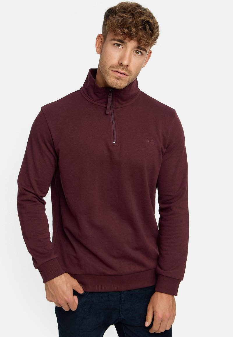 Burgunderfarbener Reißverschluss-Sweatshirt mit hohem Kragen, gerippten Bündchen und Saum, mit einem dezenten Logo auf der Brust, gefertigt aus weichem Stoff.