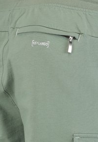 Groene katoenen joggers hebben een ritszak, geborduurd "KEY LARGO" logo en een gladde textuur, ideaal voor comfort.