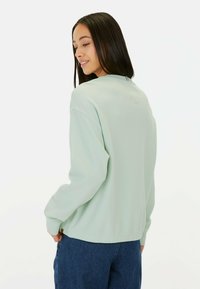 Licht muntgroene top met lange mouwen en een gestructureerd patroon, ontspannen pasvorm, geribde manchetten en een ronde onderkant. Gecombineerd met donkere denim onderkleding.