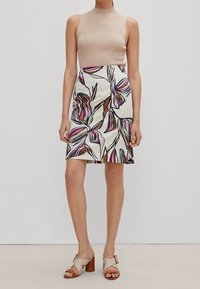 Haut sans manches beige côtelé associé à une jupe blanche à motif floral avec des accents roses et marron. Le modèle porte des sandales à talons carrés beige.