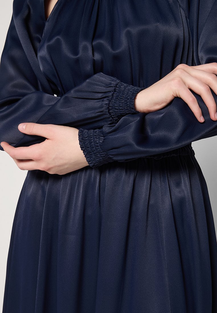 Vestito di raso blu navy con maniche a sbuffo elasticizzate e polsini smock, caratterizzato da una vita arricciata per una silhouette fluida.