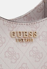 Handtas van lichtroze textiel met een goudkleurig "GUESS EST 1981" logo, subtiele reliëfpatronen en gestikte details.