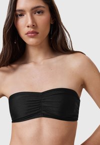 Top bandeau nero con texture arricciata, realizzato in tessuto liscio. Presenta un taglio dritto con design minimalista, offrendo una silhouette elegante.