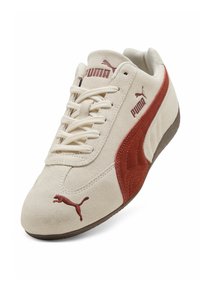 Beige σουέτ αθλητικό παπούτσι Puma με σκουριά ριγέ στο πλάι, λογότυπα Puma στη γλώσσα, το πλάι και τα δάχτυλα, και μπεζ κορδόνια σε λευκό φόντο.