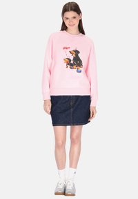 Roze trui met een cartoon van twee teckelhonden, gecombineerd met een denim rok. De trui heeft een losse pasvorm en geribbelde manchetten.