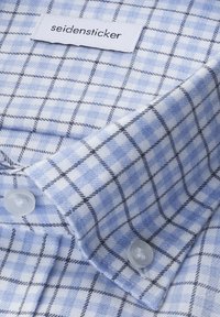 Niebiesko-biała koszula w kratę z zapięciem na guziki, z metką z tkaniny oznaczoną "seidensticker". Gładka bawełniana faktura, kontrastujące czarne linie.