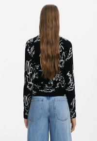 Svart tröja med grå handskriven textmönster, långa ärmar och en figurnära design. I kombination med ljusblå vida denimjeans.