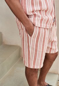 Pantalones cortos a rayas en color terracota y crema, con una tela texturizada, bolsillos laterales y cintura elástica.