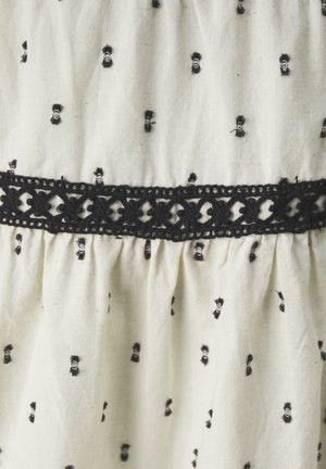 Tejido blanco con pequeños patrones bordados en forma de lazo negro, con un distintivo borde de encaje negro a lo largo de la cintura.