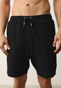 Shorts noirs à côtes, fabriqués en tissu léger, avec une taille élastique dotée d'un cordon de serrage, atteignant le milieu de la cuisse.