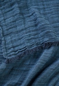 Tissu texturé en bleu foncé avec un motif tissé et des bords frangés. Présente une texture douce et lisse ainsi que des lignes horizontales à travers tout le tissu.