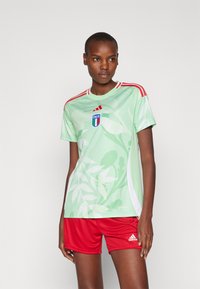 Svijetlozelena sportska majica s uzorkom lišća, crvene pruge na ramenima i grbom Italije; uparen s crvenim šortsevima s Adidas logom.