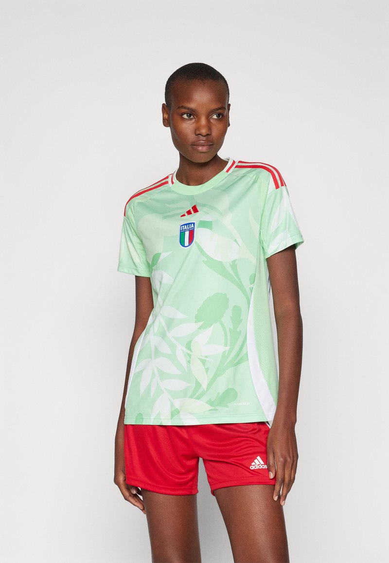 Svijetlozelena sportska majica s uzorkom lišća, crvene pruge na ramenima i grbom Italije; uparen s crvenim šortsevima s Adidas logom.