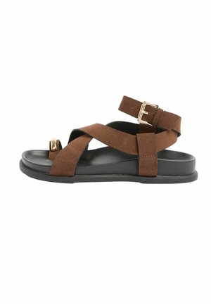 Barna velúr szandál fekete talppal, széles keresztpántokkal, lábujjgyűrűvel és arany csattos bokapánttal.