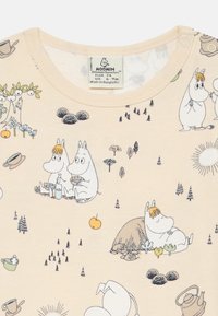 Chemise en coton beige clair à manches courtes mettant en avant des personnages Moomin dans des designs ludiques, avec des illustrations d'arbres, de fleurs et d'accessoires.