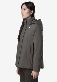 Veste isolante grise avec capuche, dotée d'une fermeture éclair, d'une grande poche avant et d'un petit logo sur la poitrine. Texture lisse et mate.