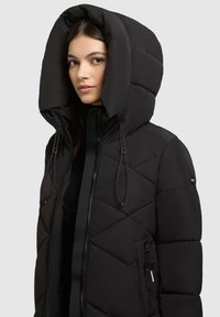 Sort polstret jakke med diamantquilt, oversized hætte, lynlåslukning, justerbare snoretræk og sidelommer med lynlås.