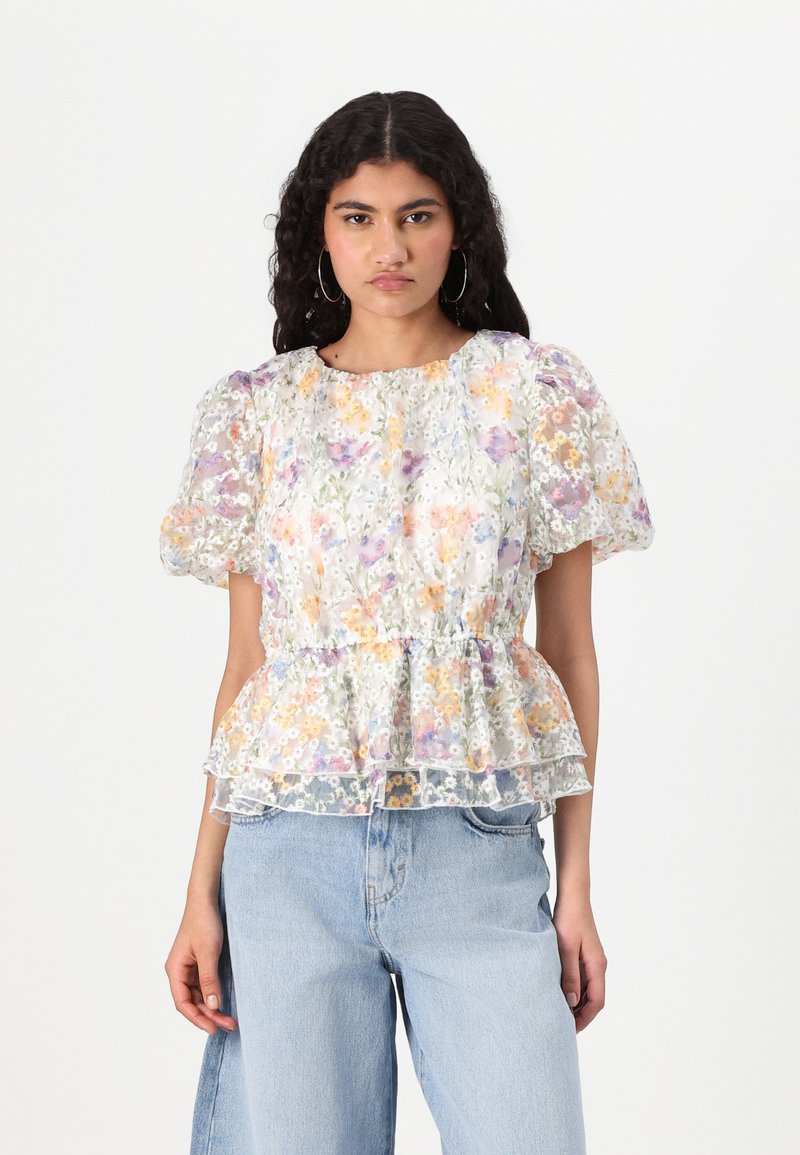 Blomstrete peplum-top i gjennomsiktig stoff, med pastellfarger, pufferm og en volangkant. Kombinert med lyseblå denimjeans.
