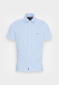 Camisa de manga corta azul claro hecha de algodón, con cuello, botones blancos y un pequeño logo en el pecho.