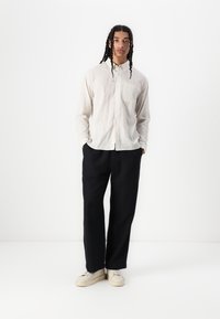 Chemise légère à boutons avec un motif à carreaux subtil, associée à un pantalon noir ample et des chaussures claires. Design simple et fonctionnel.