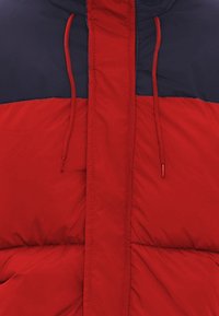 Giacca puffer rossa e blu con zip, cordini elastici, texture trapuntata e design color block sul petto.