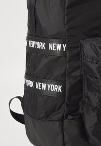 Zaino in nylon nero con più cinghie esterne con il testo "NEW YORK", tessuto testurizzato e una maniglia laterale per un facile trasporto.