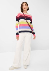 Gestreifter Pullover mit horizontalen Bändern in Pink, Marineblau, Grün und Blau; kombiniert mit weiten weißen Hosen und hellen Sneakers.