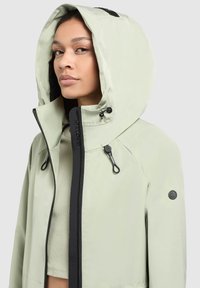Light green waterproof jacket with a hood, contrasting black zipper and accents, and adjustable drawstrings. Featuring a logo on the sleeve.